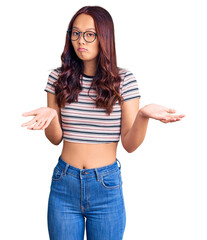 Young beautiful chinese girl wearing casual clothes clueless and confused expression with arms and...