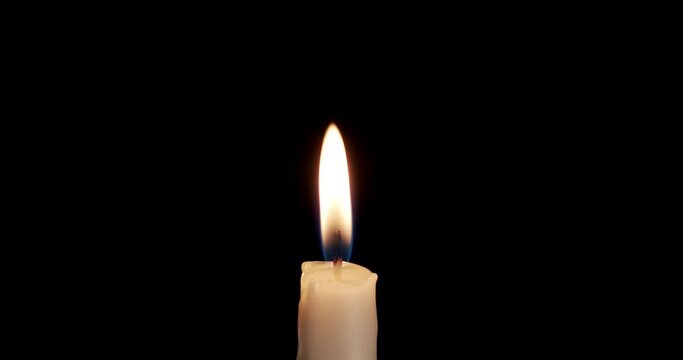 A single white candle burning.Isolated candle burning with dark background.White paraffin candle with yellow shades burns on a black background.Background or illustration of remembrance or celebration