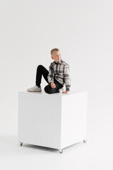 full-length boy sitting on a white cube on a white background
