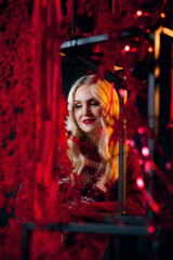 Fototapeta na wymiar A positive blonde woman in New Year's red clothes in an atmospheric photo studio with a stylish festive interior in red colors.