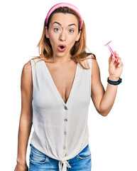 Young caucasian woman holding razor scared and amazed with open mouth for surprise, disbelief face
