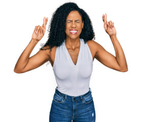 Middle age african american woman wearing casual style with sleeveless shirt gesturing finger crossed smiling with hope and eyes closed. luck and superstitious concept.