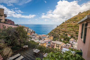 Fototapeta na wymiar Stunning view of Manarola village in Cinque Terre National Park, beautiful cityscape with colorful houses and green terraces on cliffs over a sea, Liguria region of Italy.