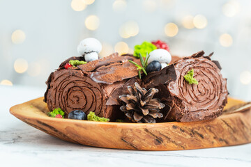 Traditional  French Christmas chocolate dessert  BûchedeNoël (Yule log). Christmas festive pastry in the shape of a log on the white background with blurred bokeh lights