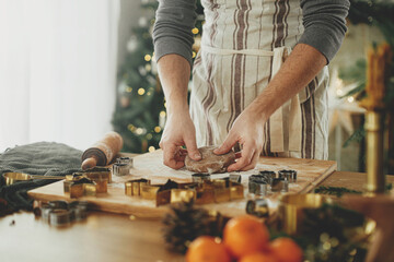 Hands kneading gingerbread dough with rolling pin, cooking spices, festive decorations on rustic table against stylish christmas tree. Man making christmas gingerbread cookies, holiday time - obrazy, fototapety, plakaty