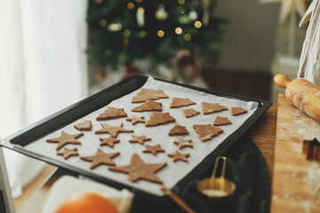 Raw gingerbread cookies in festive shapes on baking tray on rustic table with holiday decorations...