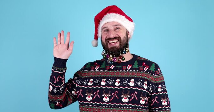 Hello! Portrait of positive handsome bearded man in santa hat and sweater waving raised hand and saying hi to camera, christmas time.