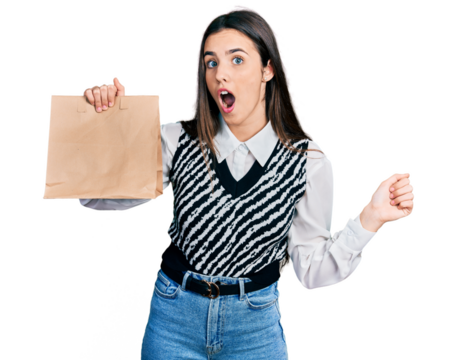 Young brunette teenager holding take away paper bag scared and amazed with open mouth for surprise, disbelief face