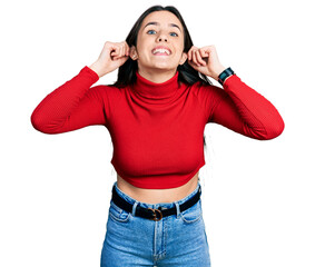 Young brunette teenager wearing red turtleneck sweater smiling pulling ears with fingers, funny...