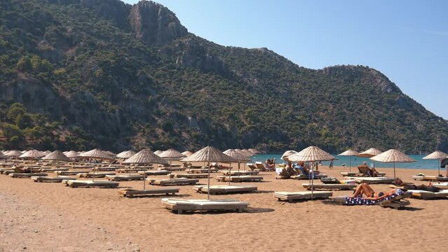 IZMIR, TURKEY - SEPTEMBER 1, 2023: Group of people enjoying relaxing beach day on patara beach, sunbathing and relaxing by sea, admiring picturesque mountain landscape on sunny day.
