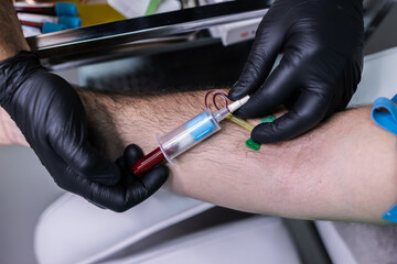 Focused photo of two hands with black gloves performing a blood draw on the arm of his patient.
