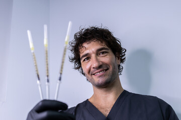 Portrait of a doctor with a smile on his face while holding three syringes in his right hand.