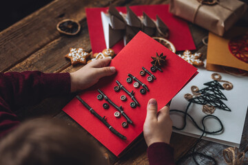 Concept of christmas leisure, family time, do it yourself present. Little boy holding handmade card made with recyclable natural materials, zero waste, sustainable lifestyle, hobby