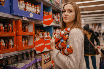 Stack of Chocolate Santa Clauses. Christmas time. A young woman chooses a gift set for Christmas to a child on a supermarket shelf.