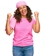 Obraz na płótnie Canvas Middle age hispanic woman wearing breast cancer support pink scarf screaming proud, celebrating victory and success very excited with raised arms