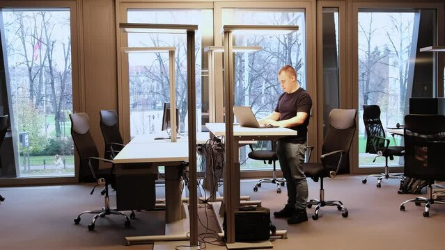 The programmer typing in laptop raises table and works standing. Adjustable Height Desk Stand In Office. Working atmosphere. Comfortable working conditions. 