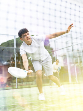 Sportive young man playing padel with partner on tennis cort in spring. View through tennis net