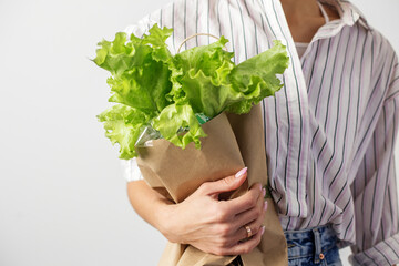 Female hands hold a packet with lettuce on a gray background. Organic food.