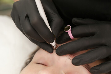 Microblading artist  in a black gloves mixing pigment in ink ring cup. Close-up of pigment ring container and ink for eyebrow tattoo. Beauty procedure preparation.