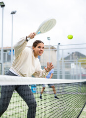 Emotional young female paddle tennis player preparing to perform forehand to return ball on outdoor...