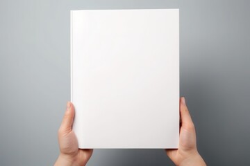 Blank white book or magazine held in hands against a grey background, perfect for mockups and graphic design presentations.
