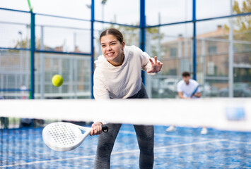 Portrait of young female in sportswear enjoying popular sport padel game on tennis court outside