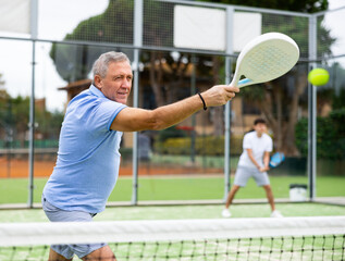 View through the tennis net at an elderly player in the game of padel