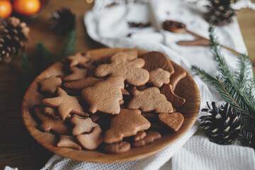 Christmas gingerbread cookies in wooden plate on rustic table with fir branches, pinecone, napkin....