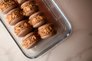 Brown macaroons decorated with cornflakes lie in a glass container, top view