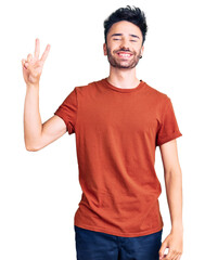 Young hispanic man wearing casual clothes smiling with happy face winking at the camera doing victory sign. number two.