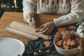 Decorating gingerbread cookies with icing on rustic wooden table close up. Atmospheric Christmas...