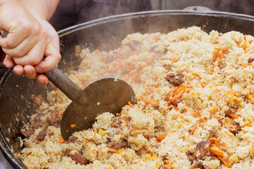 Preparation of tasty traditional Uzbek pilaf in cauldron at street food festival