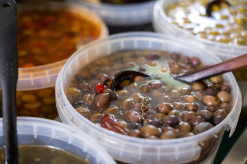 Pickled black olives scooped with skimmer out of bucket put on sale counter in the market