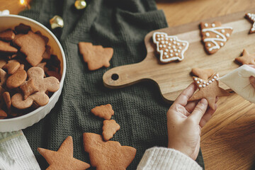 Decorating gingerbread cookies with icing on rustic wooden table top view. Atmospheric Christmas...