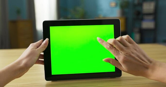 Video captures a woman comfortably seated on couch in her living room holds a tablet in her hands, and the screen displays a vibrant green mockup, indicating that she is actively using the device.