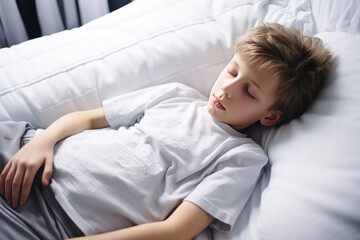 Child toddler boy is sad lying on the bed and holding his stomach. Abdominal pain in children, symptoms of gastritis, poisoning and intestinal infection, abdominal bloating. - obrazy, fototapety, plakaty