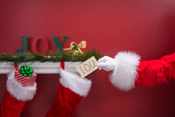 Santa Claus placing an IOU note into Christmas stocking hanging from mantle