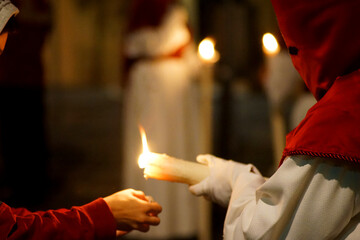 A Nazarene giving a candle to a child during Holy Week   - obrazy, fototapety, plakaty