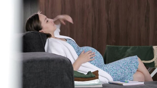 Pregnant woman strokes her stomach, after which she wants to get up from the sofa.