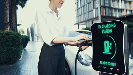 Businesswoman recharge her electric car from charging station at city center or public parking car....