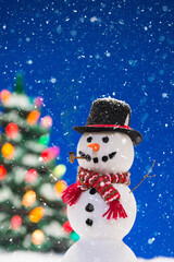 A happy snowman wearing a top hat with Christmas tree in background while snowing