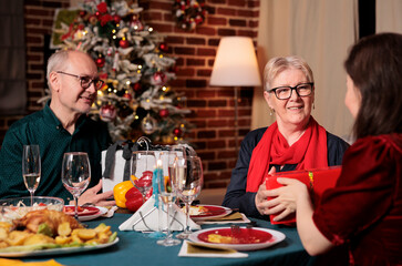 Daughter giving gift to her mother at christmas dinner event, feeling happy during winter celebration holiday. Family exchanging presents and enjoying good time at table with people.