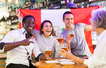 Happy international sport supporters holding up the flag of Peru and drinking beer in the pub