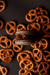 Brown macaroon with chocolate cream lies among scattered pretzels