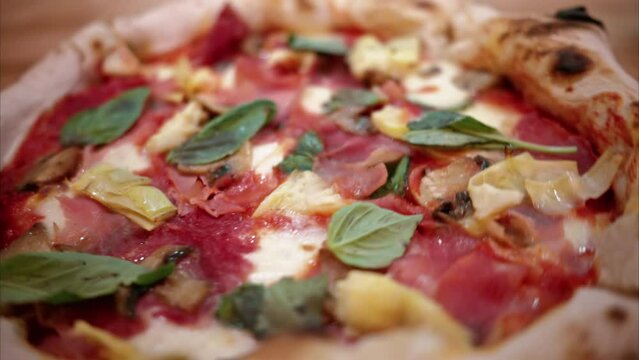 Close view of capricciosa pizza on a plate in an italian restaurant with prosciutto, artichoke, cheese and basil