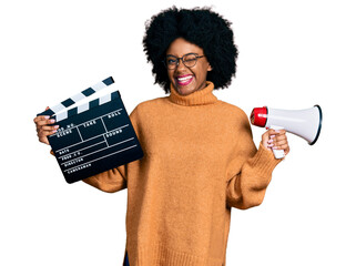 Young african american woman holding video film clapboard and megaphone winking looking at the...