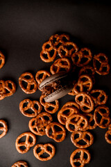 One brown macaroon with chocolate cream lies among scattered pretzels