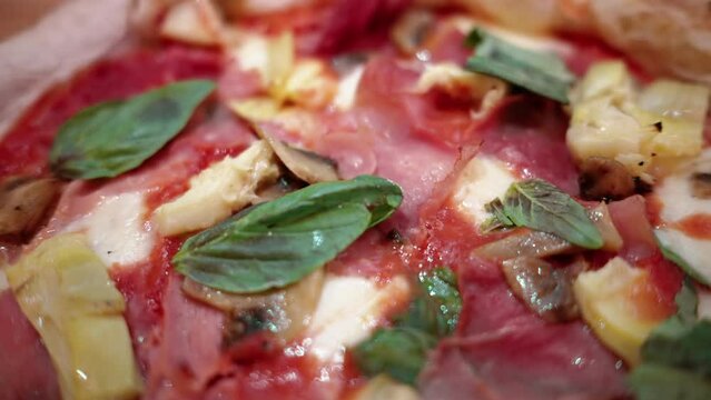 Close view of capricciosa pizza on a plate in an italian restaurant with prosciutto, artichoke, cheese and basil
