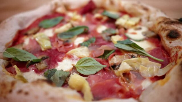 Close view of capricciosa pizza on a plate in an italian restaurant with prosciutto, artichoke, cheese and basil
