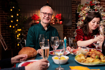 Grandpa at dinner table with family eating traditional meal and celebrating christmas holiday at home. Senior adults meeting together at festive gathering during winter seasonal event.